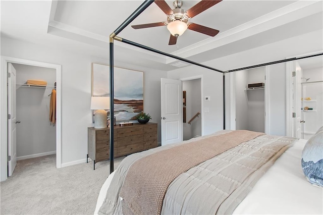 bedroom featuring a walk in closet, a closet, light carpet, and a tray ceiling