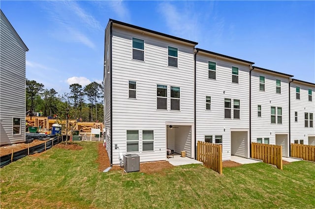 rear view of house with fence, central AC unit, and a yard