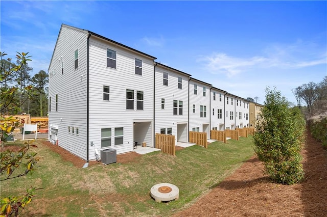 back of property with central AC unit, a lawn, and fence