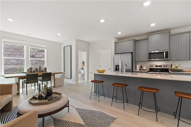 kitchen with recessed lighting, gray cabinets, appliances with stainless steel finishes, a sink, and a kitchen bar