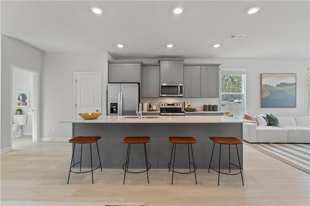 kitchen featuring a breakfast bar area, gray cabinetry, stainless steel appliances, a sink, and a large island with sink