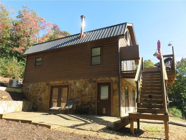 back of house featuring a wooden deck, stone siding, a patio, french doors, and stairs