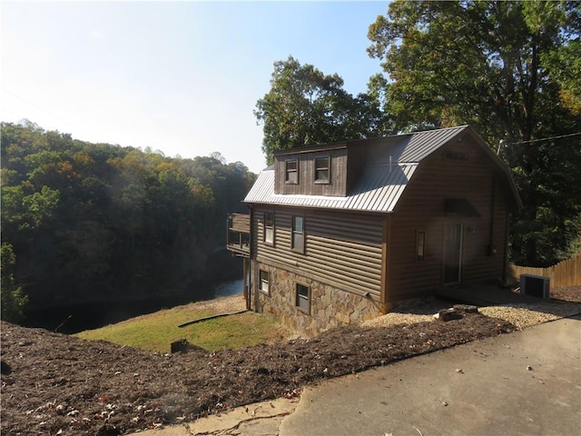 view of side of home with central air condition unit, stone siding, and metal roof