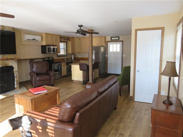 living room featuring a fireplace, a ceiling fan, a wall mounted AC, and light wood-style floors