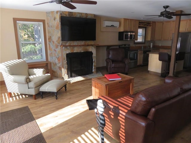 living room with ceiling fan, a wall mounted AC, a stone fireplace, and light wood finished floors