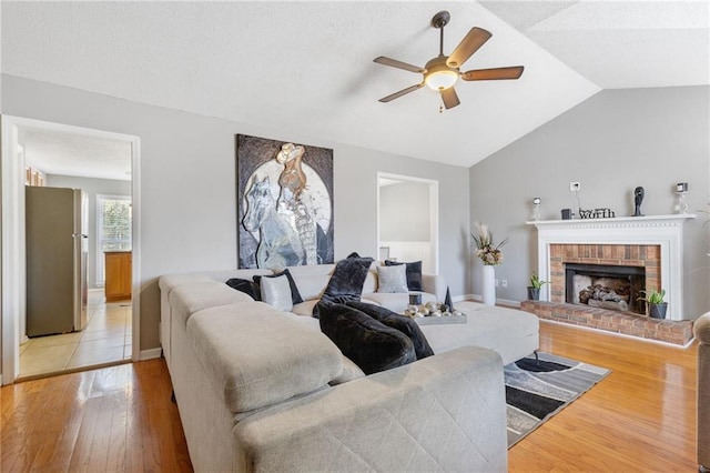 living room with ceiling fan, vaulted ceiling, light wood-type flooring, and a brick fireplace