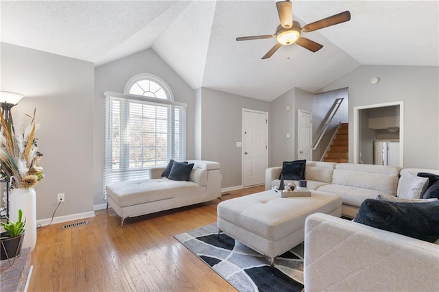 living room featuring vaulted ceiling, a textured ceiling, ceiling fan, and light wood-type flooring