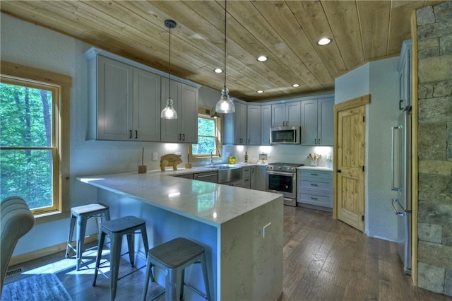 kitchen with appliances with stainless steel finishes, a breakfast bar, hanging light fixtures, kitchen peninsula, and wooden ceiling