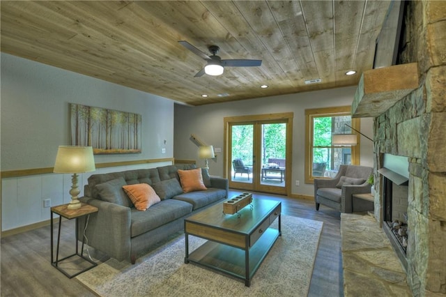 living room with hardwood / wood-style flooring, a stone fireplace, wooden ceiling, and ceiling fan