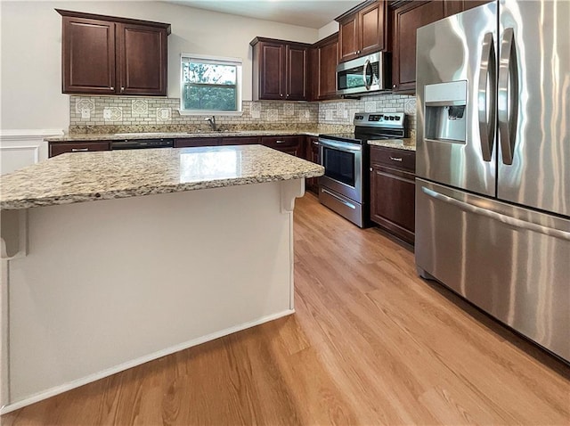 kitchen with light stone counters, light hardwood / wood-style flooring, a kitchen island, and stainless steel appliances