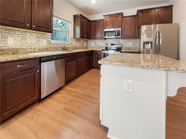 kitchen featuring a center island, sink, light stone countertops, light wood-type flooring, and appliances with stainless steel finishes