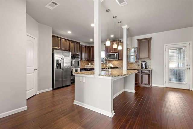 kitchen with a kitchen island, appliances with stainless steel finishes, decorative light fixtures, light stone countertops, and dark wood-type flooring