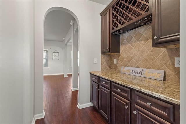 kitchen featuring light stone countertops, dark brown cabinets, backsplash, and dark hardwood / wood-style flooring