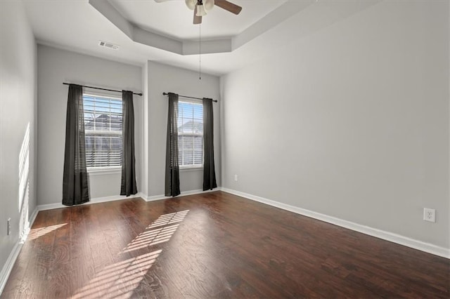 spare room featuring dark wood-type flooring, ceiling fan, and a tray ceiling