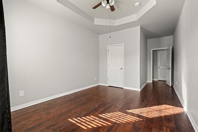 unfurnished bedroom featuring dark hardwood / wood-style flooring, a tray ceiling, and ceiling fan