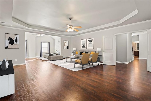 living room with a raised ceiling, dark wood-type flooring, and ceiling fan