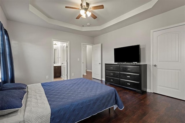 bedroom with a raised ceiling, ceiling fan, dark hardwood / wood-style flooring, and ensuite bath