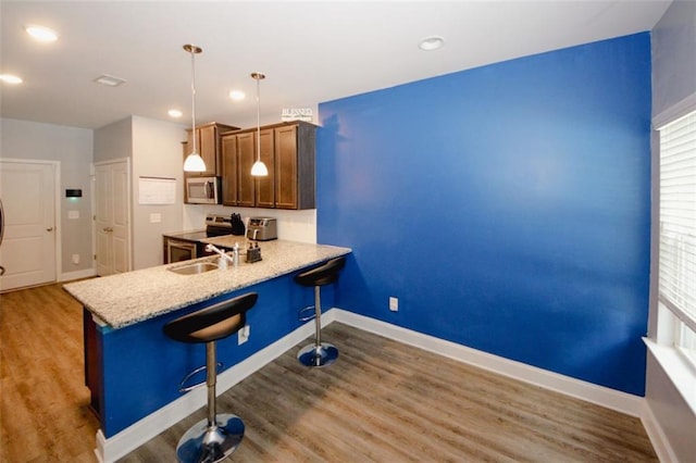 kitchen featuring stainless steel appliances, a sink, a kitchen bar, wood finished floors, and decorative light fixtures