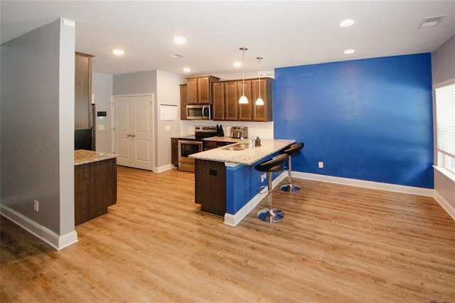 kitchen featuring stainless steel appliances, a breakfast bar area, baseboards, a peninsula, and light wood finished floors