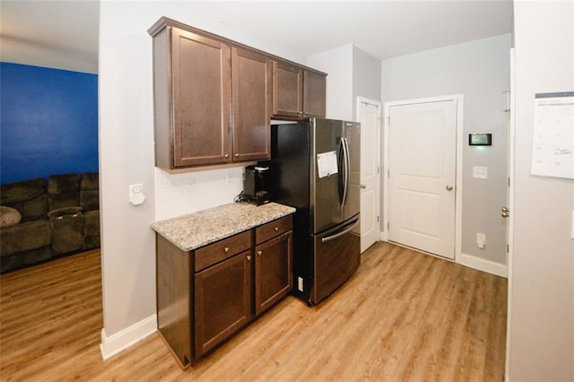 kitchen with freestanding refrigerator, light wood-type flooring, dark brown cabinets, and baseboards