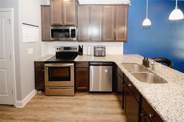 kitchen with stainless steel appliances, light wood-style flooring, a sink, hanging light fixtures, and light stone counters
