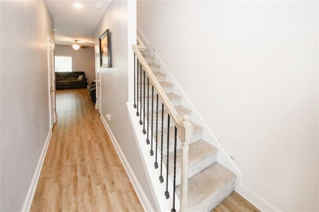 staircase featuring wood finished floors, a ceiling fan, and baseboards