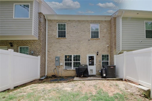 back of house with brick siding, a fenced backyard, and central AC unit