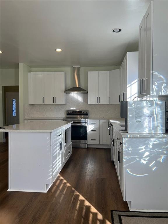 kitchen with wall chimney range hood, dark hardwood / wood-style flooring, backsplash, electric stove, and white cabinets