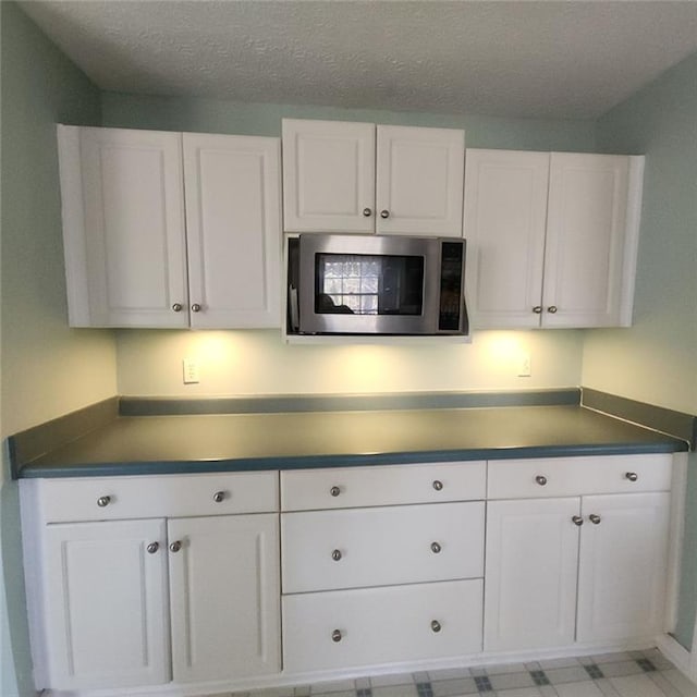 kitchen featuring stainless steel microwave, white cabinets, dark countertops, and a textured ceiling