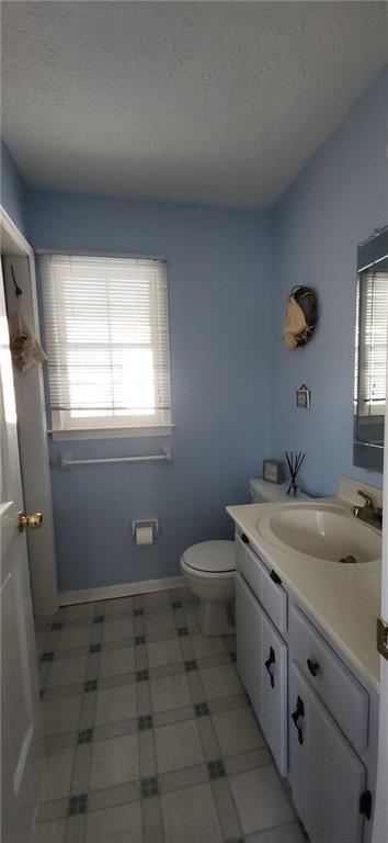 bathroom with baseboards, toilet, vanity, and a textured ceiling