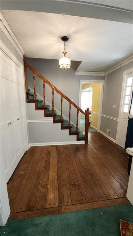 stairs with an inviting chandelier, hardwood / wood-style flooring, baseboards, and ornamental molding