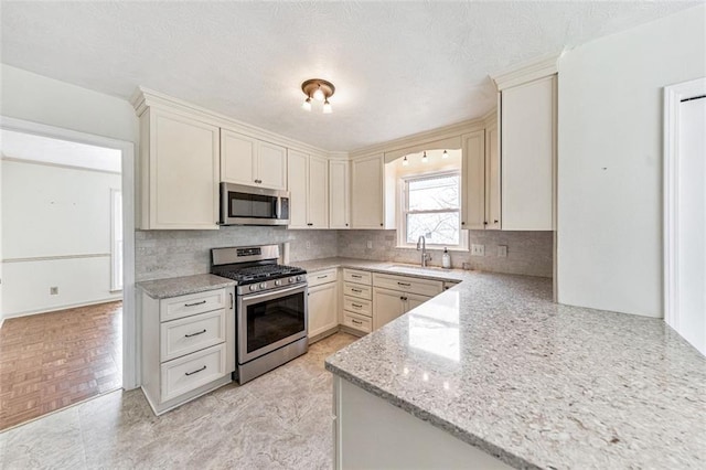 kitchen with tasteful backsplash, light stone counters, stainless steel appliances, and a sink