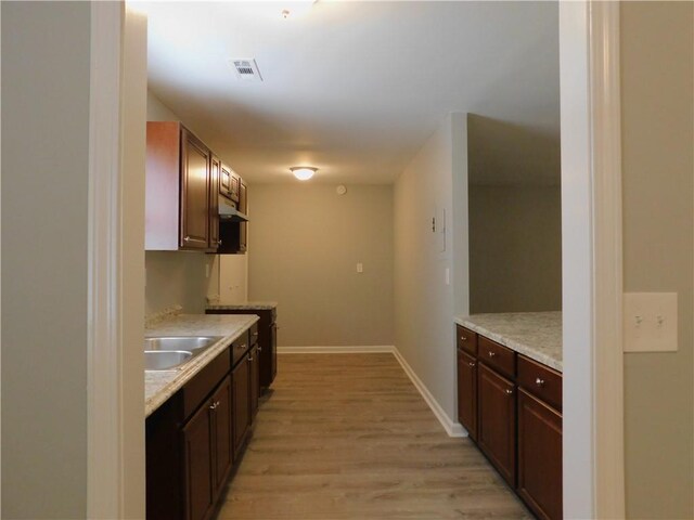 kitchen featuring sink, light stone counters, dark brown cabinets, light hardwood / wood-style flooring, and black dishwasher