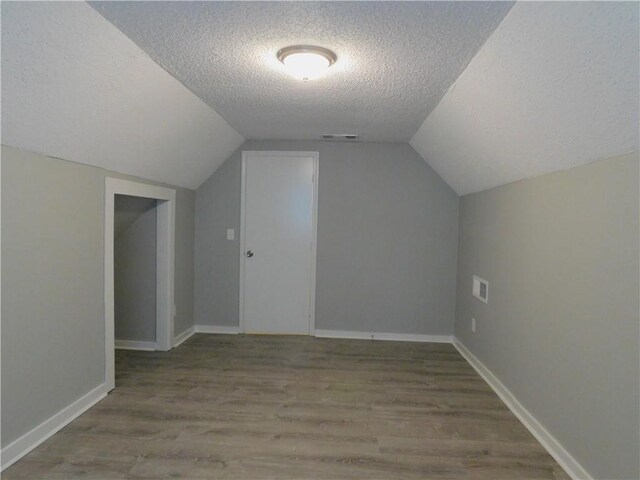 additional living space featuring hardwood / wood-style floors, a textured ceiling, and vaulted ceiling