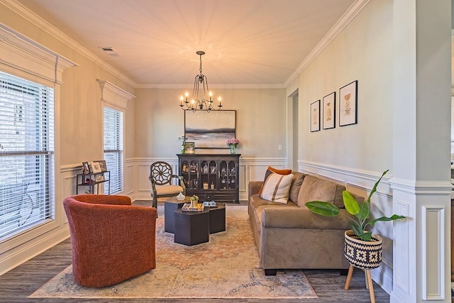living area with visible vents, a wainscoted wall, ornamental molding, wood finished floors, and an inviting chandelier