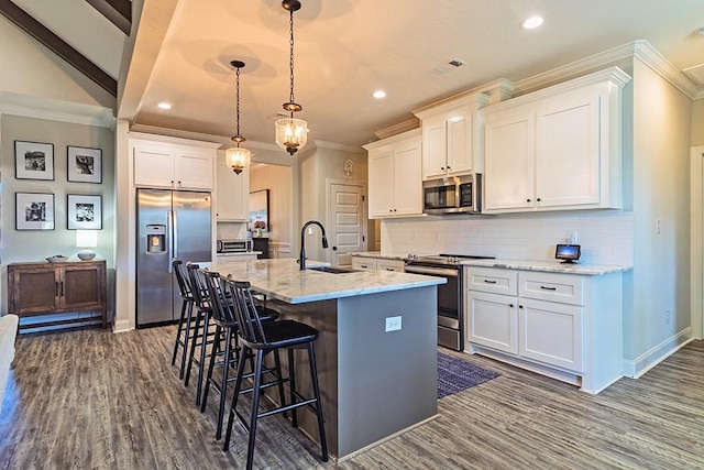 kitchen with a kitchen island with sink, a sink, stainless steel appliances, white cabinets, and a kitchen breakfast bar