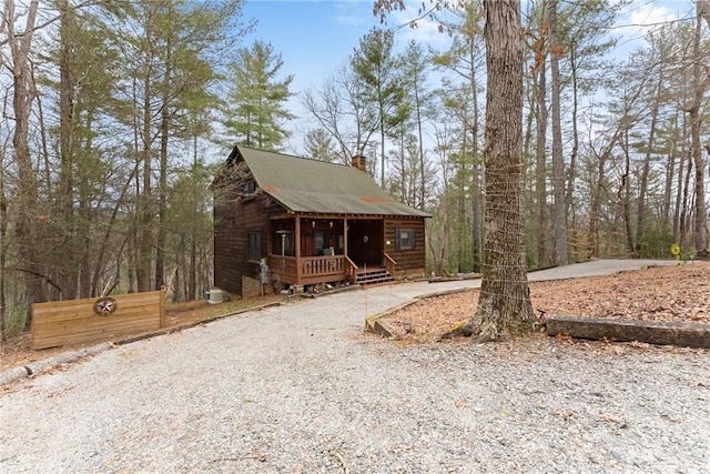 chalet / cabin featuring gravel driveway, covered porch, and a chimney