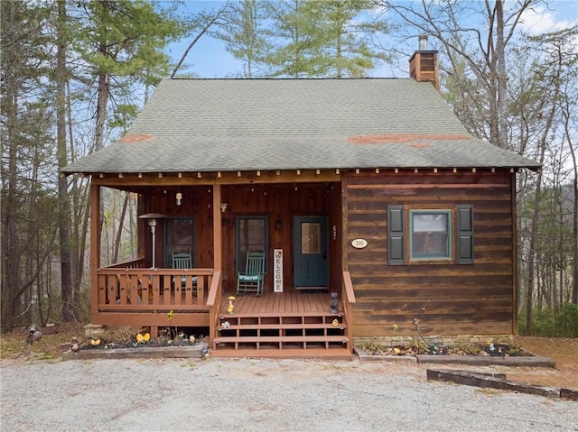 chalet / cabin with a porch, roof with shingles, and a chimney