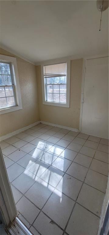 unfurnished room with a wealth of natural light, light tile patterned flooring, lofted ceiling, and baseboards