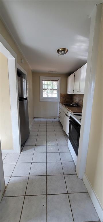 kitchen with backsplash, electric range, freestanding refrigerator, white cabinetry, and light tile patterned flooring