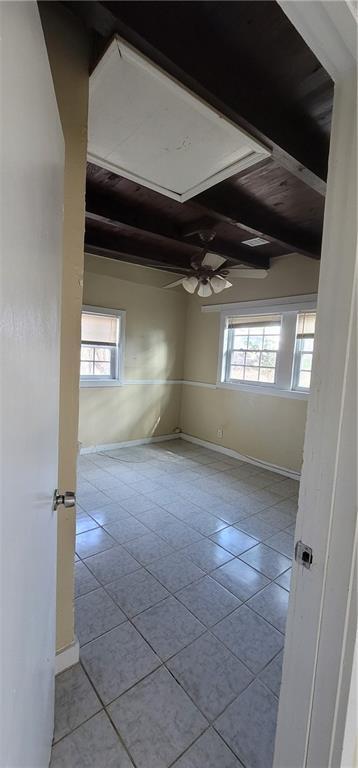 tiled empty room featuring a wealth of natural light, a ceiling fan, baseboards, and beam ceiling