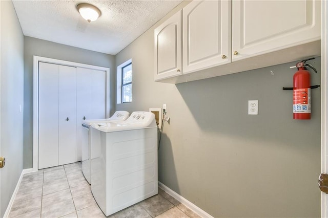 clothes washing area featuring cabinets, light tile patterned floors, a textured ceiling, and washer and clothes dryer