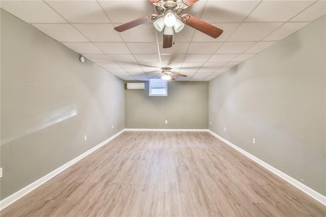 basement with a paneled ceiling, light wood-type flooring, and an AC wall unit