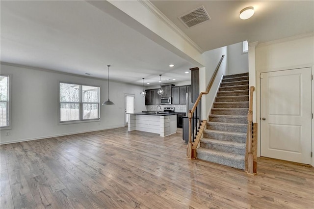 unfurnished living room featuring light wood-type flooring, visible vents, stairway, crown molding, and baseboards