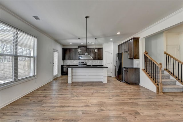 kitchen with visible vents, dark countertops, freestanding refrigerator, light wood finished floors, and dark brown cabinets