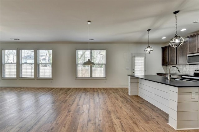 kitchen with a sink, dark countertops, backsplash, open floor plan, and stainless steel appliances