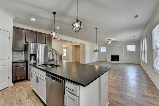 kitchen with dark countertops, crown molding, a fireplace, stainless steel appliances, and a sink