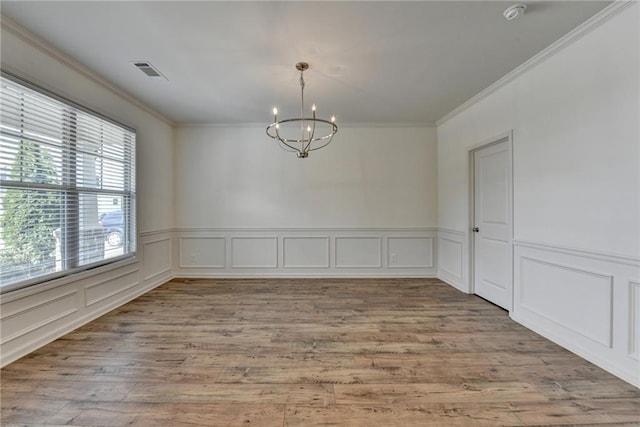 empty room with visible vents, ornamental molding, light wood-style flooring, an inviting chandelier, and a decorative wall