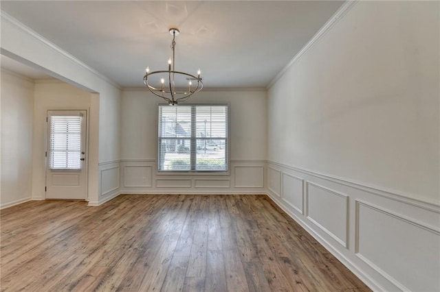 unfurnished dining area featuring a decorative wall, crown molding, an inviting chandelier, and wood finished floors