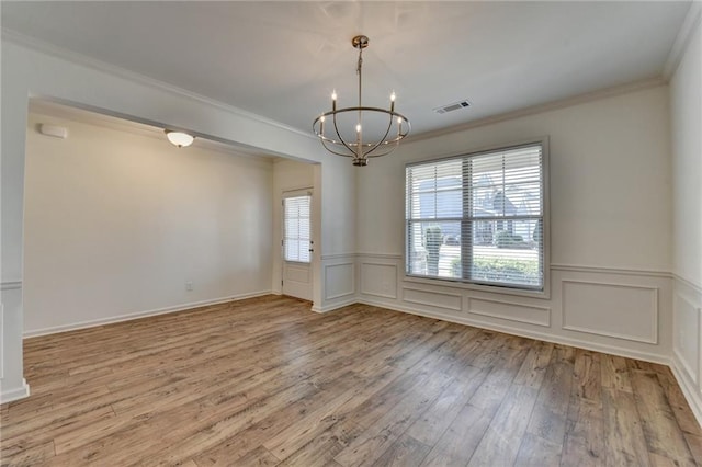 empty room featuring visible vents, wood-type flooring, crown molding, a decorative wall, and a chandelier